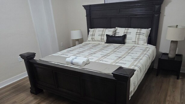 A bedroom with a dark wooden bed, white walls, a ceiling fan, and a window with blinds. - Modern Heart of Hollywood (Hollywood)