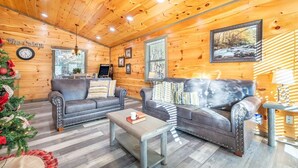 A cozy log cabin interior with two leather sofas, a coffee table, a fireplace, and a clock on the wall. - Eagles Nest Hideaway (Cosby)