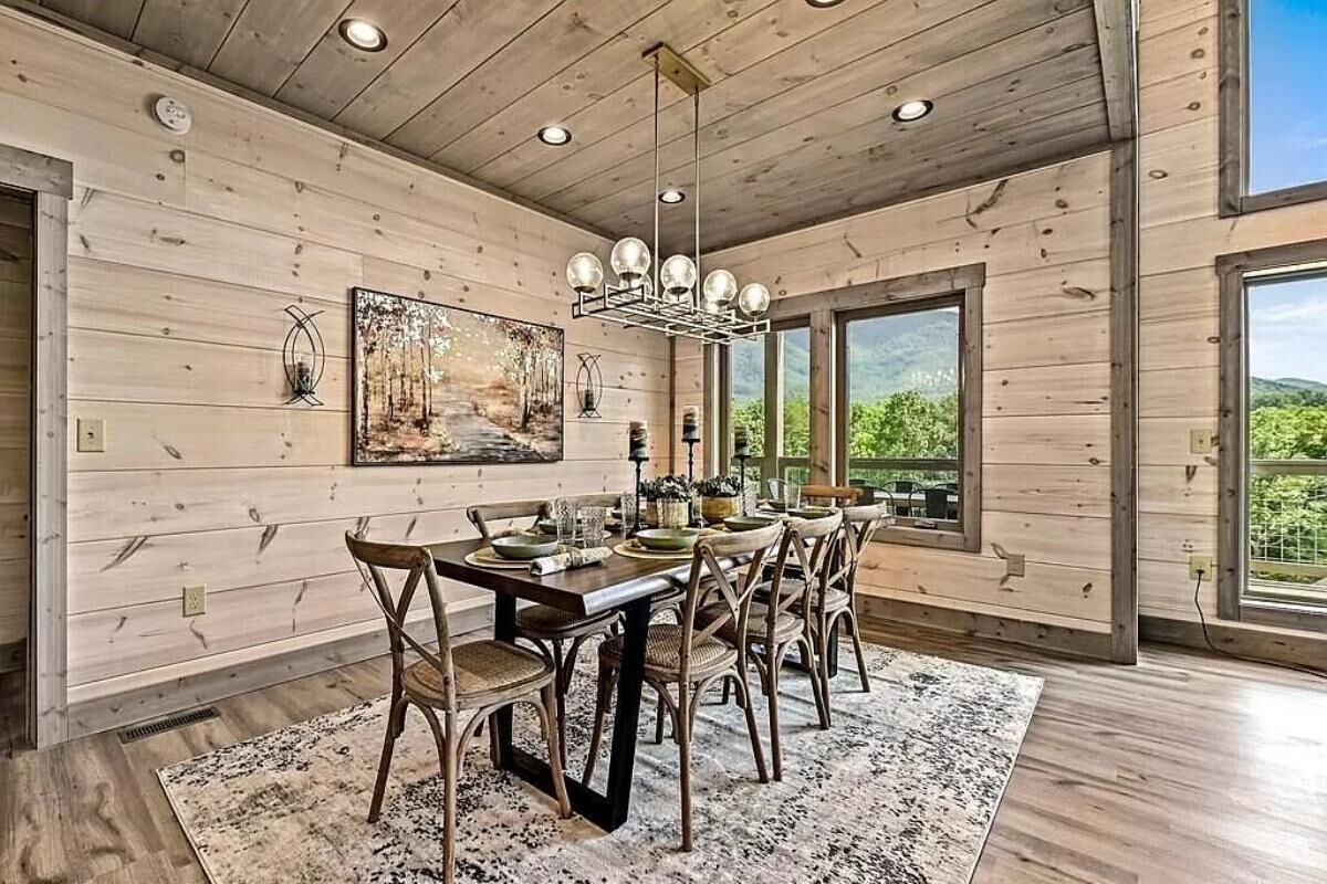 A dining area with a wooden table, chairs, a chandelier, and a painting on the wall.