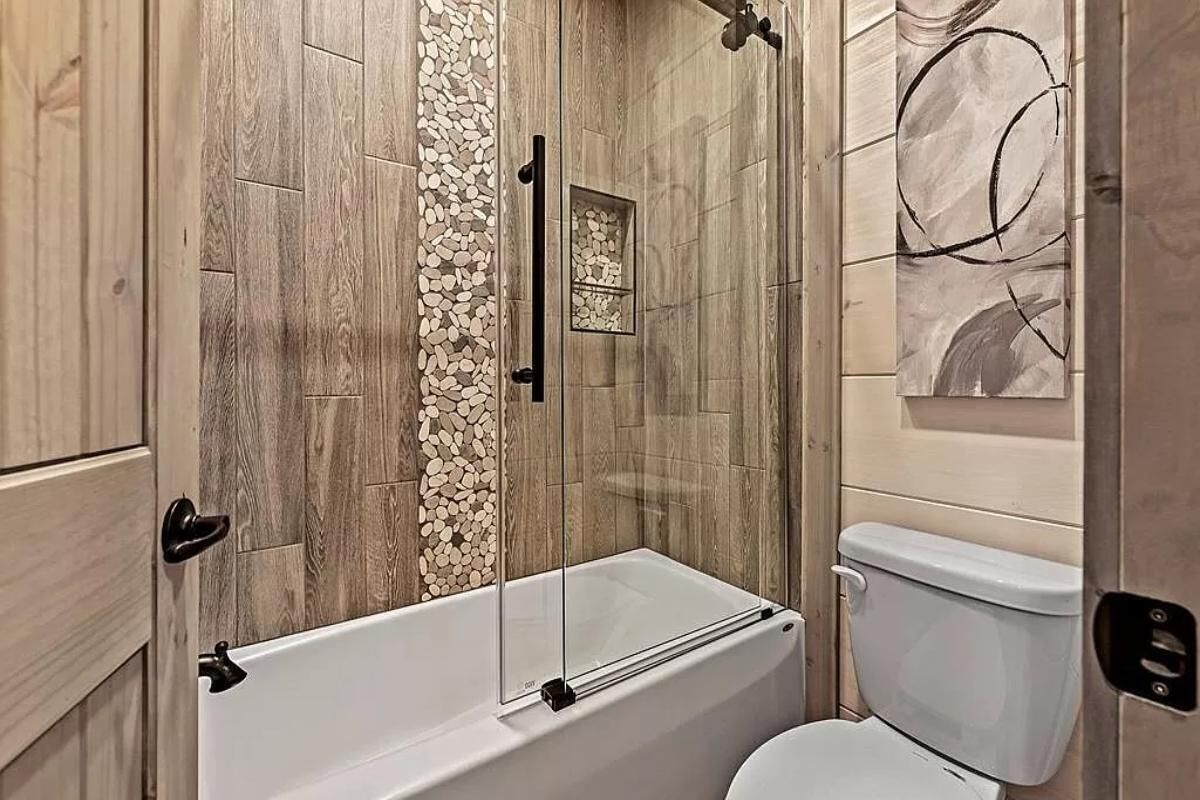 Un baño con cabina de ducha de vidrio, inodoro y pared de madera con detalles de piedras.