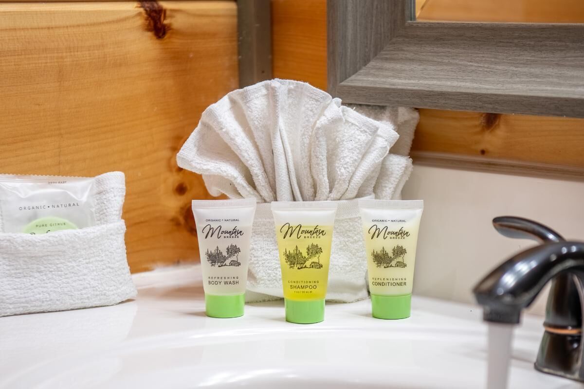 Een badkamer met een houten wand, een witte handdoek en drie Mountain Breeze producten: douchegel, shampoo en conditioner.