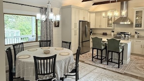 A modern kitchen with white cabinetry, a central island, and a dining area with a round table and chairs. - Private Pond, Mountain Escape (Highlands)