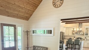 A spacious living area with a large rug, a wooden bench, a clock, and a view into the kitchen. - Private Pond, Mountain Escape (Highlands)