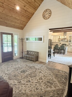 A spacious living area with a large rug, a wooden bench, a clock, and a view into the kitchen. - Private Pond, Mountain Escape (Highlands)