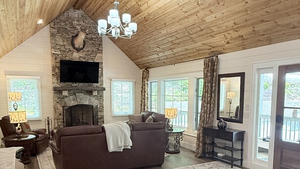 A spacious living room with a stone fireplace, wooden ceiling, and a large rug. - Private Pond, Mountain Escape (Highlands)