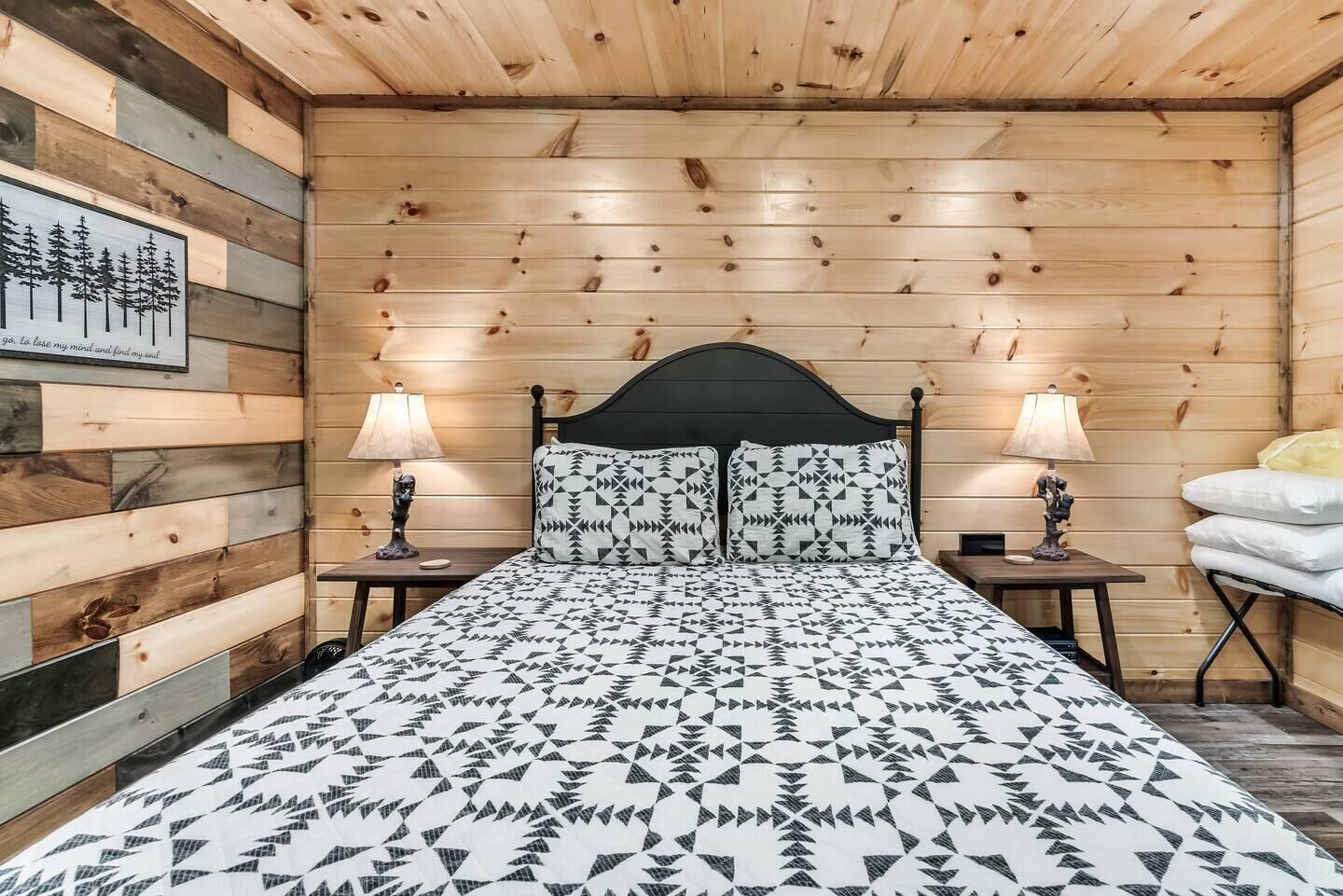 Une pièce aux murs lambrés, comprenant un lit, deux tables de chevet et une lampe fixée au mur.