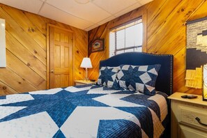 Ein Zimmer mit Holzwänden, einem Bett, einem Nachttisch, einer Lampe und einem Fenster.