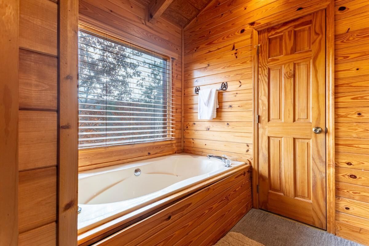 Ein Interieur einer Holzhütte mit einer Holzwanne, einem Fenster mit Jalousien und einer Tür.