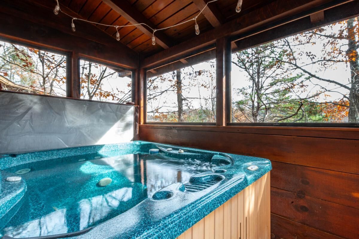 A hot tub with a wooden deck, large windows, and a view of trees.