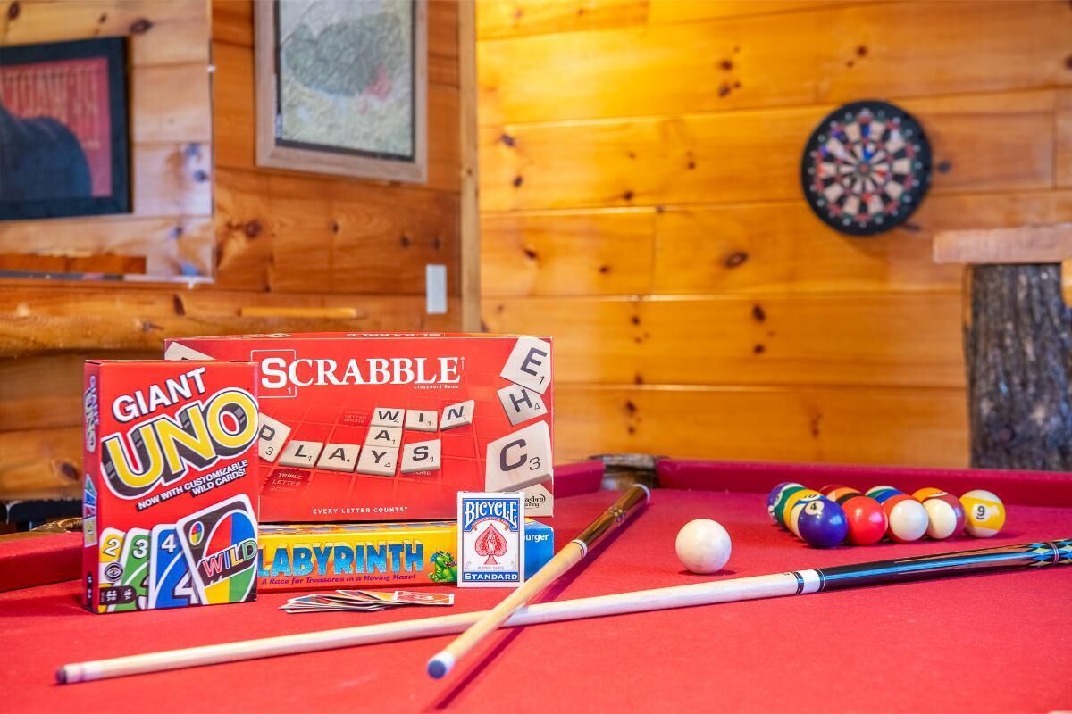 Een pooltafel met biljartballen, een keu en twee spelletjesdozen: Scrabble en Giant UNO.