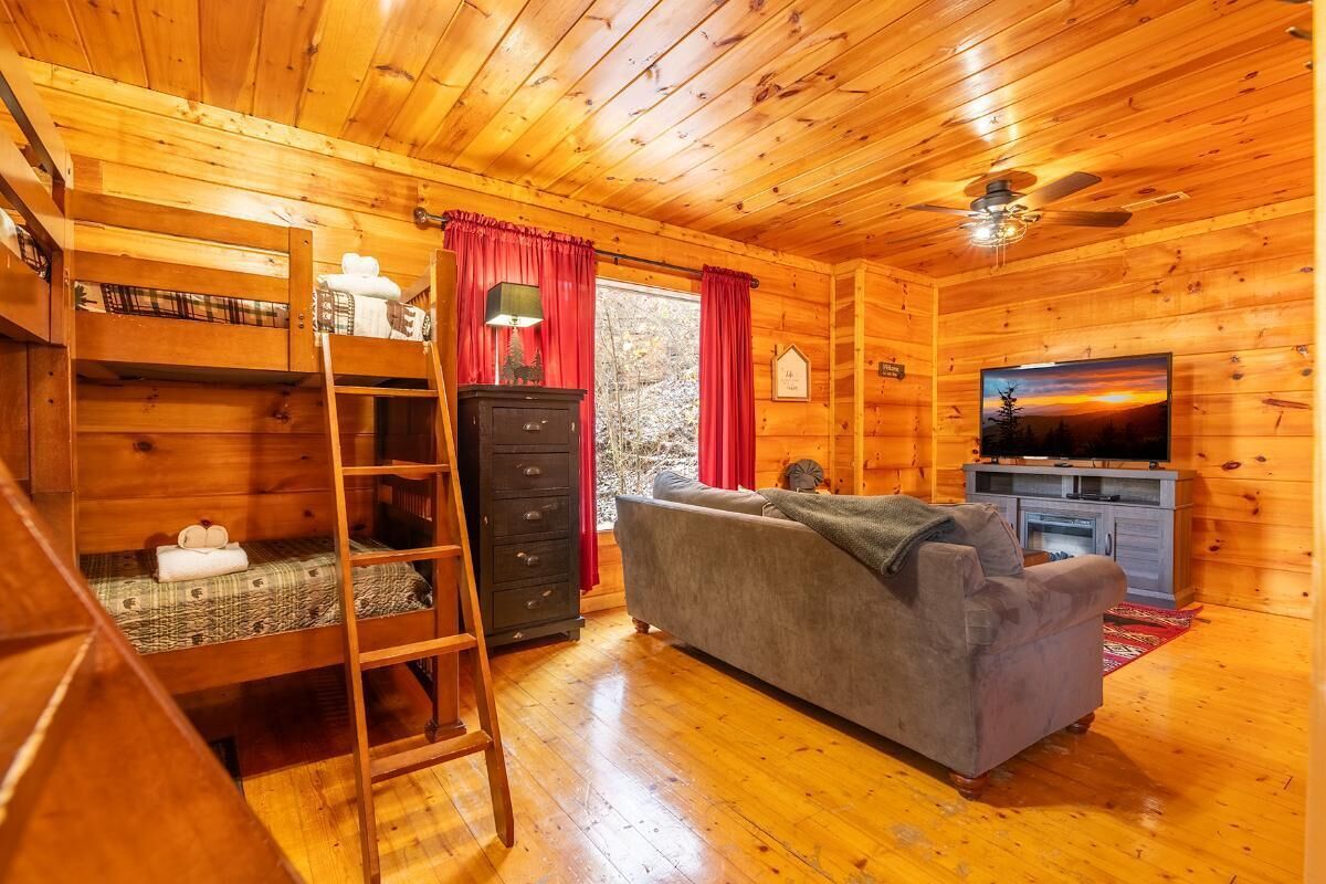Ein Interieur einer Holzhütte mit Etagenbetten, einer Couch, einem Fernseher und einem Kamin.