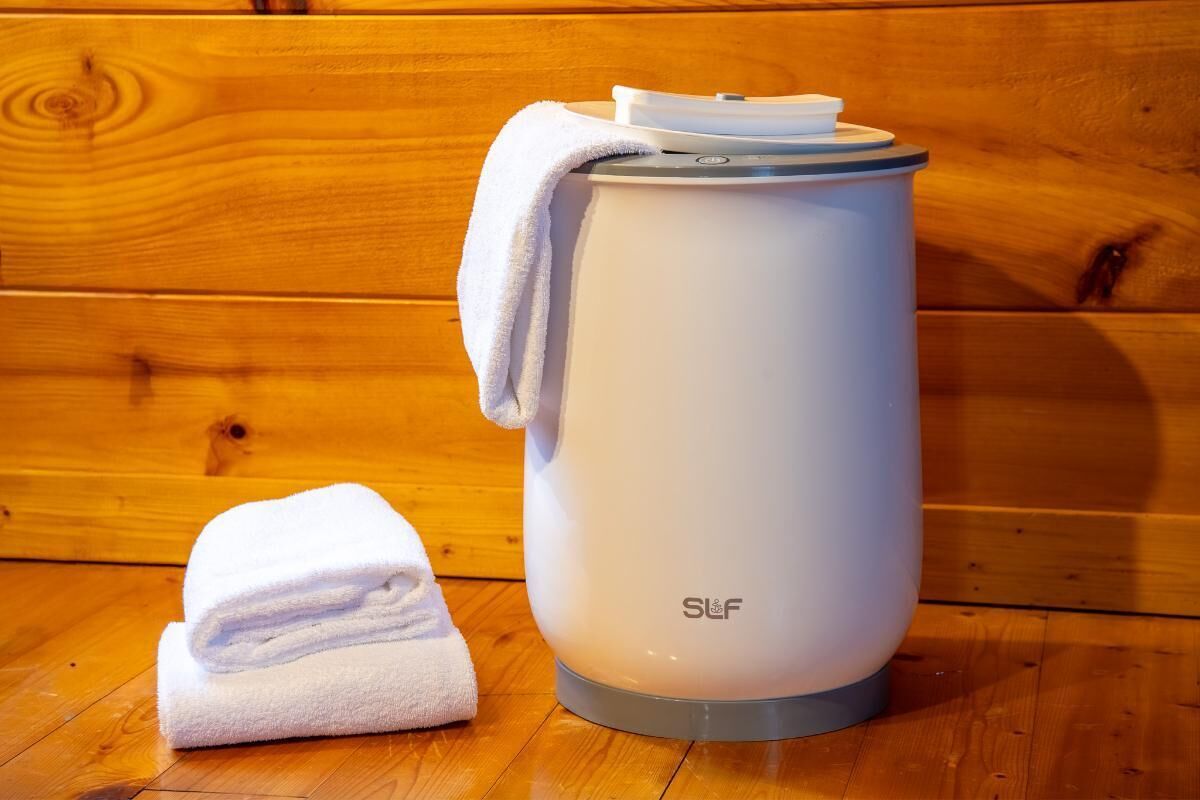 A white portable heater with a gray base, labeled 'SLF,' and a folded white towel beside it, placed on a wooden floor.