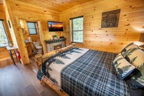 A log cabin bedroom with a bed, a fireplace, a television, and a bathroom. - Z - Heavenly Views Hideaway (Sevierville)