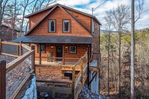 A wooden cabin with a balcony, a fireplace, and a view of the surrounding forest. - Pine Haven Cabin (Sevierville)