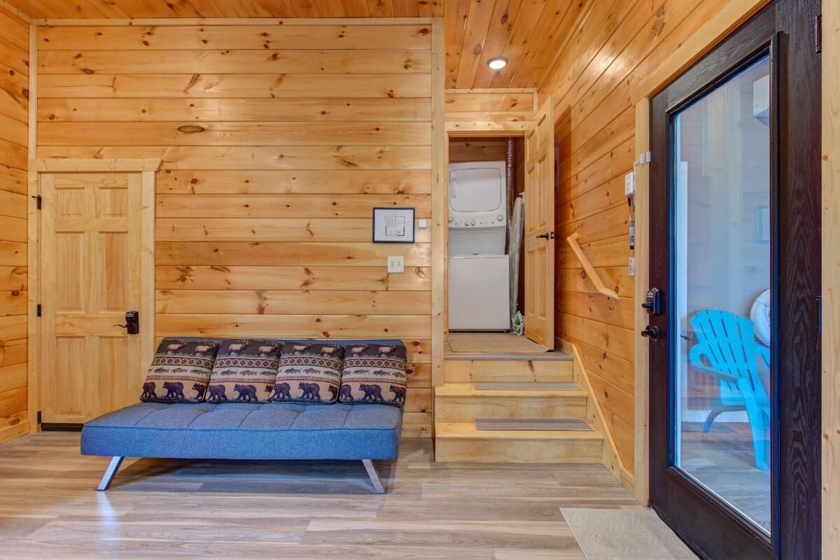 A wooden interior with a sofa, a door, and a view of a blue chair outside.