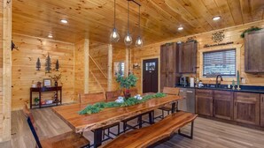 A wooden interior with a dining table, benches, pendant lights, and a kitchen area. - Pine Haven Cabin (Sevierville)