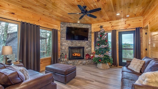 A cozy living room with a fireplace, leather sofas, a ceiling fan, and a Christmas tree. - Pine Haven Cabin (Sevierville)