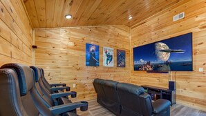 A wooden-paneled room with a large flat-screen TV, reclining chairs, and posters on the wall. - Pine Haven Cabin (Sevierville)