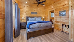 A wooden cabin bedroom with a bed, nightstands, a ceiling fan, and a painting on the wall. - Pine Haven Cabin (Sevierville)