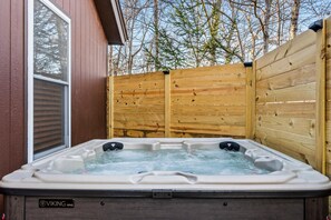 Ein Whirlpool mit Holzzaun und Fenster, umgeben von Bäumen.