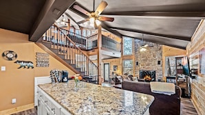 A spacious living area with a large granite island, a fireplace, and a multi-level wooden staircase. - Z - Honey Bear Treehouse (Gatlinburg)