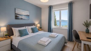 Een hotelkamer met een bed, nachtkastjes, een bureau, een stoel, een raam met gordijnen en een schilderij aan de muur.