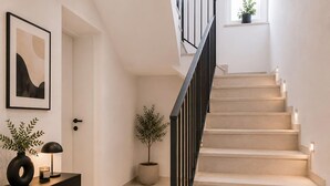 Eine Treppe mit schwarzer Geländer, ein Blumentopf, ein gerahmtes abstraktes Gemälde und ein Schreibtisch mit Lampe und Kerze.
