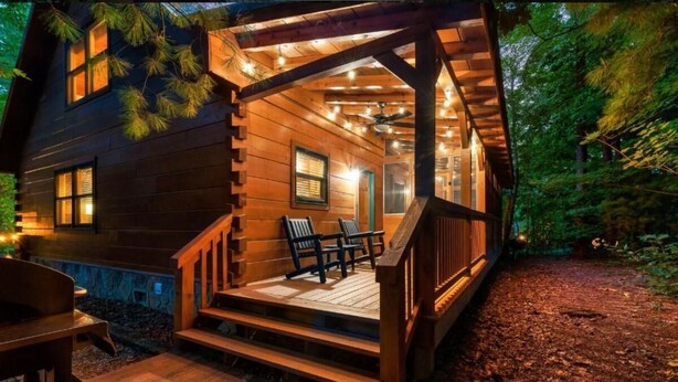 A wooden cabin with a porch, outdoor seating, and string lights. - Awesome Adventures (Sevierville)
