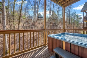 Eine Holzterrasse mit Whirlpool, umgeben von Bäumen und Häusern im Hintergrund.
