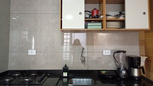 Una cocina con estufa a gas, un lavamanos, una cafetera y un armario con vajilla.