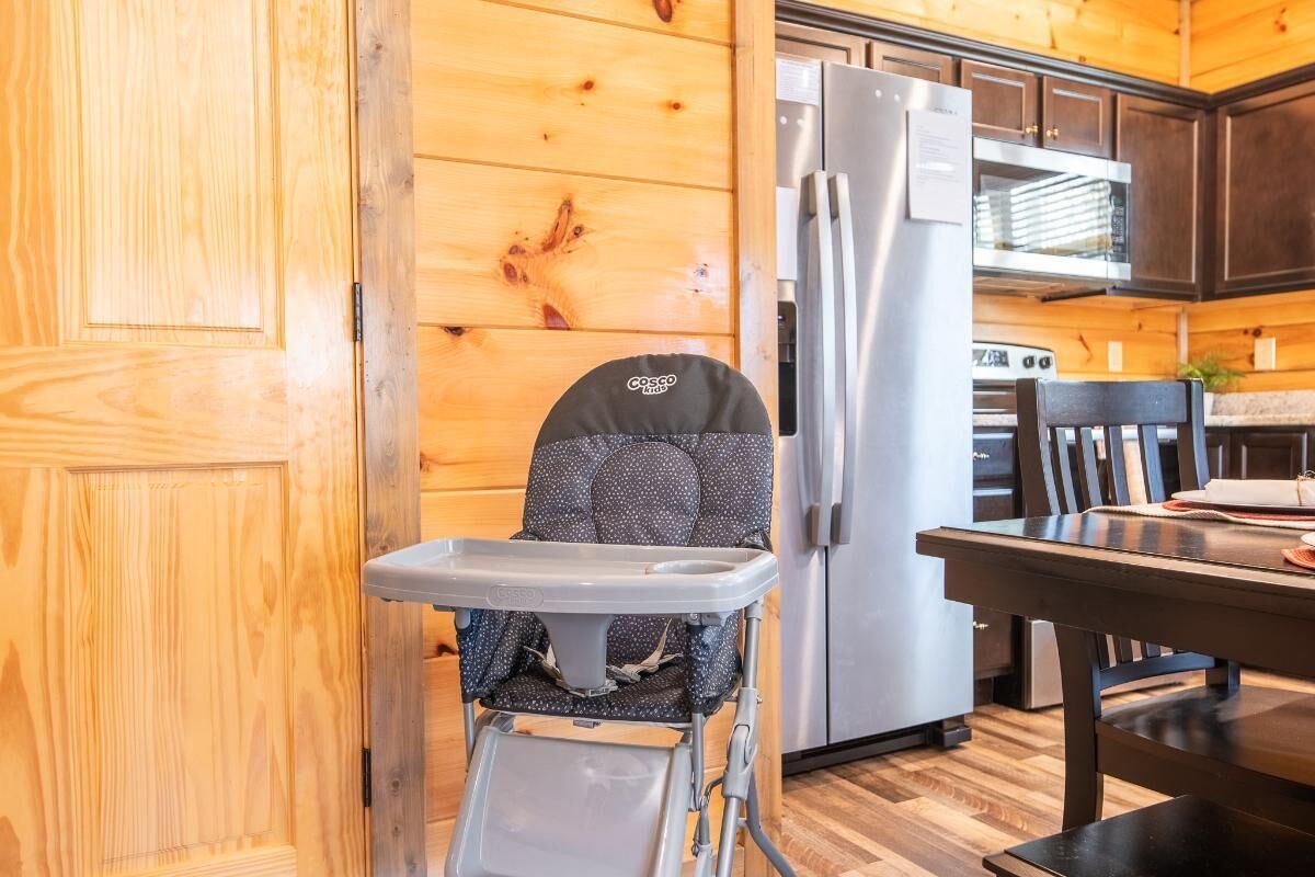 A wooden interior with a high chair, a refrigerator, and a dining table.