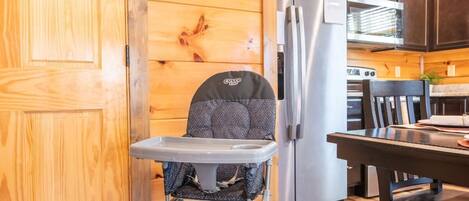 A wooden interior with a high chair, a refrigerator, and a dining table.