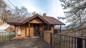 A small wooden cabin with a sloped roof, a front door, and a fenced driveway. - Blue Mist Vista (Gatlinburg)
