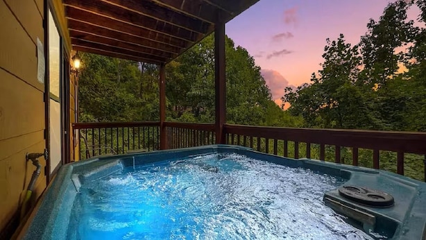 A hot tub under a wooden deck with a view of trees and a sunset. - Blue Mist Vista (Gatlinburg)