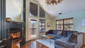 A living room with a fireplace, a sofa, a coffee table, and a large window. - Blue Mist Vista (Gatlinburg)