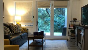 Ein Wohnzimmer mit Sofa, Couchtisch und TV-Möbel, einem Deckenventilator und Blick durch Glastüren in einen Garten.