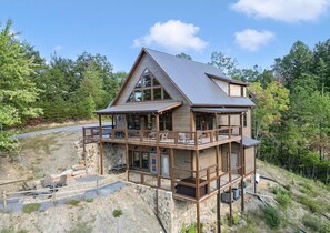 A two-story cabin with a balcony, stone foundation, and a view of the surrounding forest. - Misty Shadows (Sevierville)