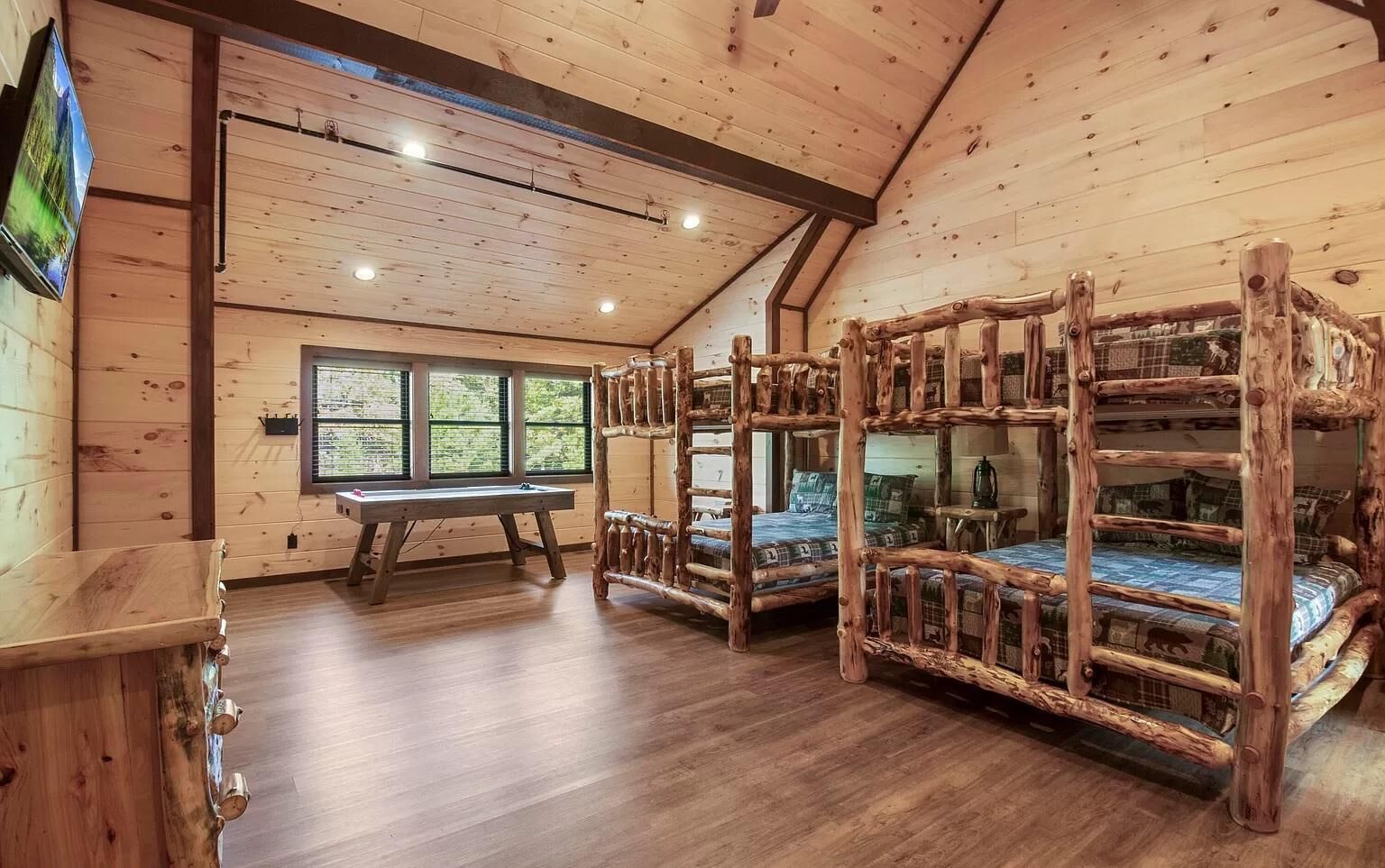 Ein rustikales Blockhaus-Interieur mit Holzbettställen, einem Holztisch und einem Fenster mit Blick auf Grün.