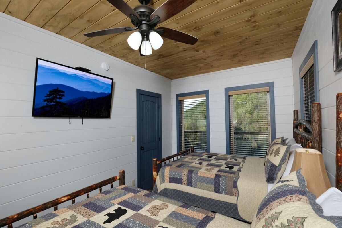 A bedroom with a bed, a ceiling fan, a TV, and a window.