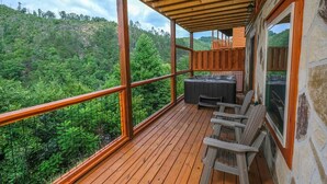 A wooden deck with a hot tub, chairs, and a view of a forested hillside. - Splash N' Love Shack (Sevierville)