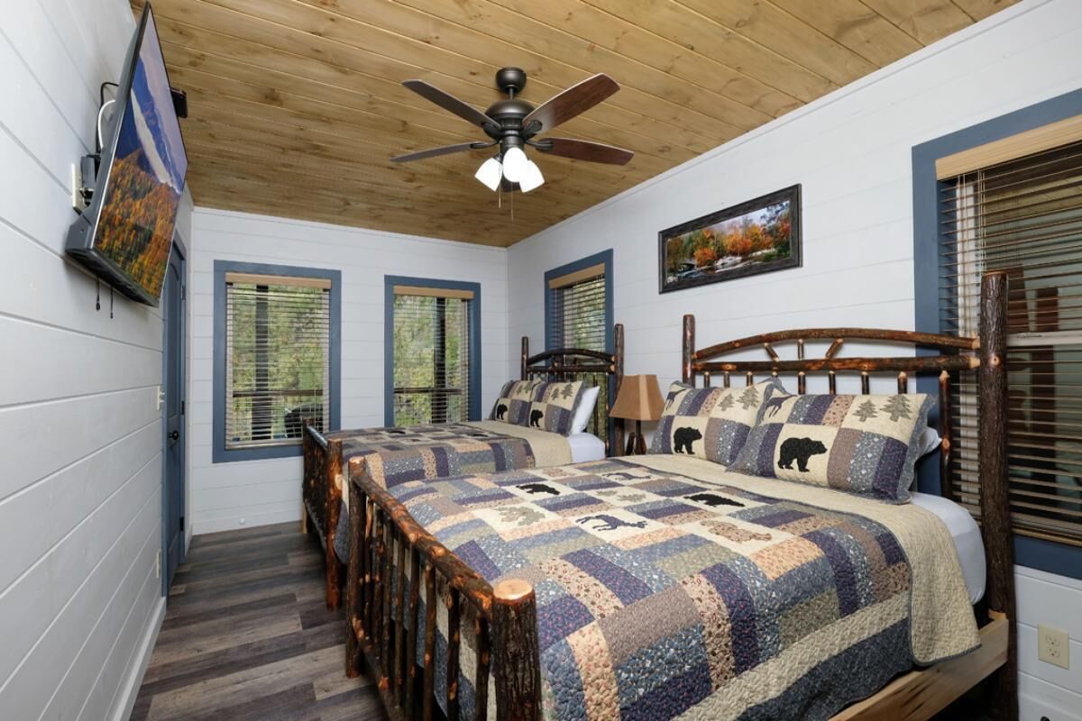 A bedroom with a wooden ceiling fan, two beds with matching headboards, a wooden table, and a wall-mounted TV.