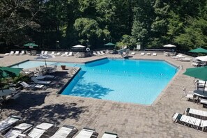 A rectangular swimming pool with a tiled deck, surrounded by lounge chairs and umbrellas. - Smoky Mountain Game Den (Gatlinburg)