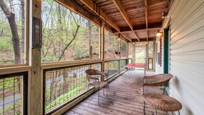 A covered porch with wicker chairs, a table, and a view of a wooded area. - Smoky Mountain Game Den (Gatlinburg)