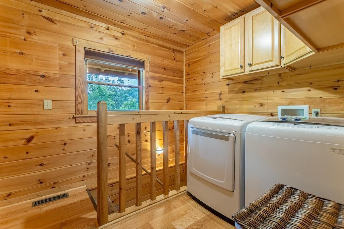 A wooden cabin interior with a washing machine, a window, and a wooden railing.