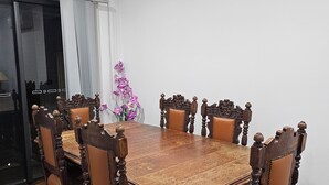 Una sala da pranzo con un grande tavolo in legno circondato da sei sedie, un vaso con fiori viola e una porta vetrata che dà su un balcone.