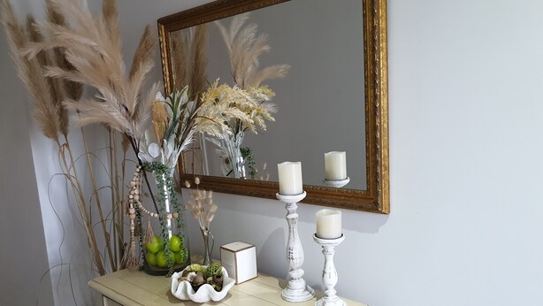 Un comò vintage con specchio, candele e piante decorative.
