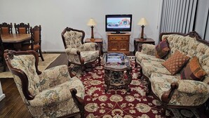 Un soggiorno con televisione, due poltrone, un divano, un tavolino da caffè e un tappeto decorato.