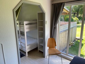 Une chambre avec un lit superposé, une chaise et une grande fenêtre donnant sur une terrasse en bois et de la verdure.