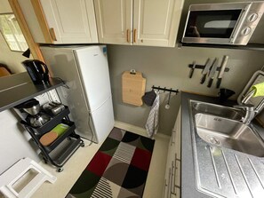 A compact kitchen with a refrigerator, microwave, sink, and a coffee maker on a cart. - 4 Star Holiday Home in Onsala (Gottskar)