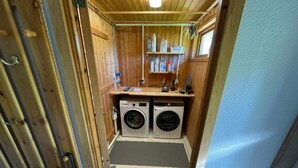 Een kleine wasruimte met twee voorladers, een plank met schoonmaakmiddelen en een houten inrichting.